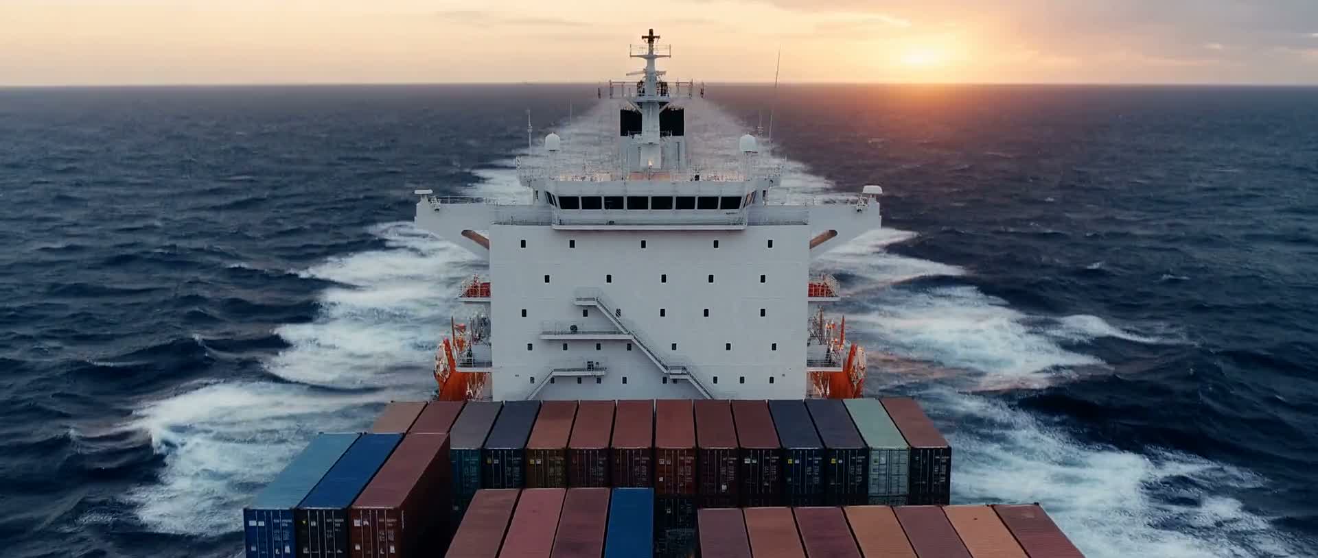 A loaded container ship seen from above her bow, under way toward the sunrise.